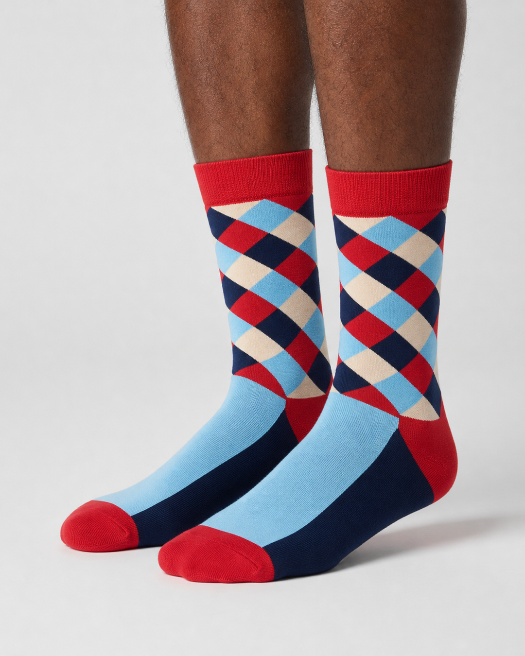 A pair of crew socks with a colorful argyle pattern on the upper leg and solid light blue, navy, and red sections on the lower half, shown worn on a person&