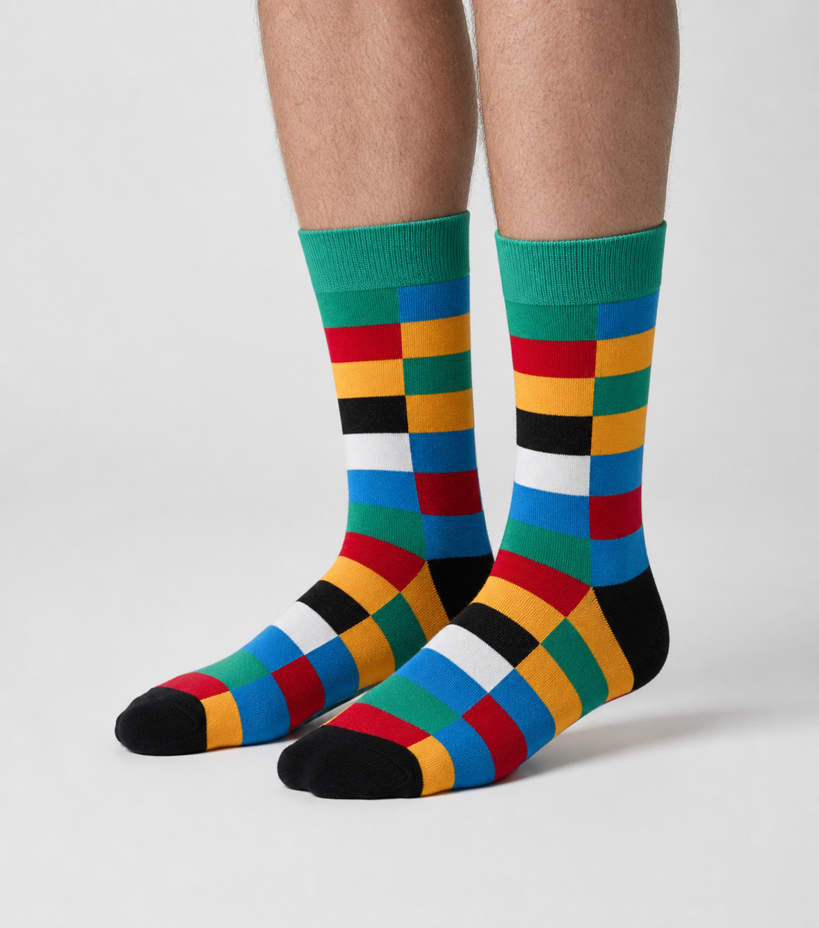 A pair of crew socks with a colorful geometric block pattern in green, blue, red, yellow, black, and white, worn on a person&